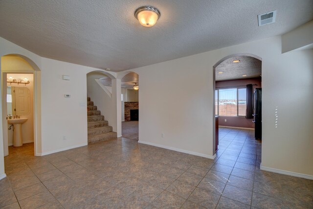 6259 Azaleas Rd NW, Albuquerque, NM 87114 - spare room with a textured ceiling, a fireplace, tile patterned flooring, stairway, and arched walkways