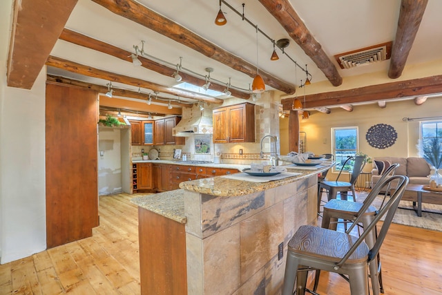 78 Quirks Ln, Corrales, NM 87048 - kitchen featuring premium range hood, brown cabinetry, stainless steel gas stovetop, light wood finished floors, and beam ceiling