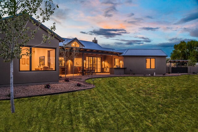 1016 Guadalupe Villa NW, Albuquerque, NM 87114 - back of house at dusk featuring a patio, stucco siding, a chimney, a yard, and fence