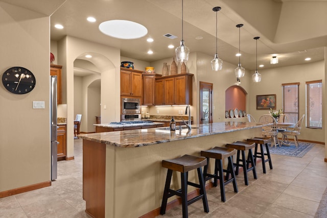 3605 Greystone Ridge Dr SE, Rio Rancho, NM 87124 - kitchen featuring appliances with stainless steel finishes, a sink, brown cabinets, a center island with sink, and arched walkways