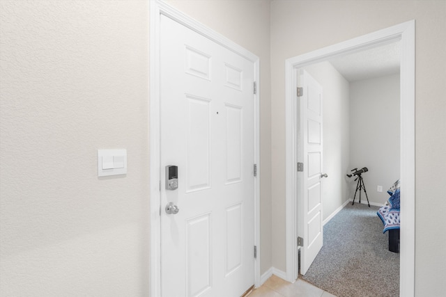 corridor featuring light tile patterned floors, baseboards, and light carpet
