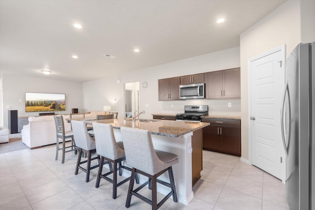 kitchen featuring a breakfast bar, light stone countertops, an island with sink, a sink, and appliances with stainless steel finishes