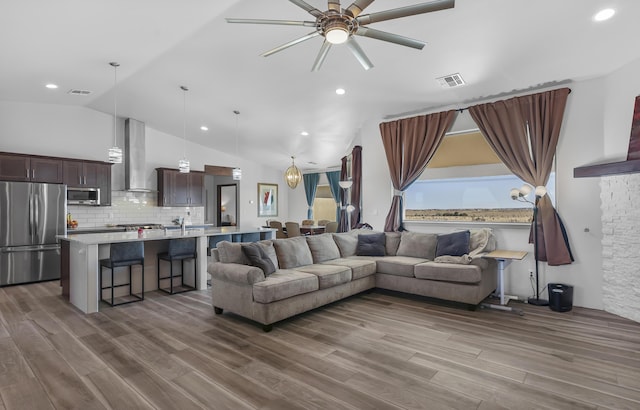 living area with wood finished floors, vaulted ceiling, a ceiling fan, and visible vents