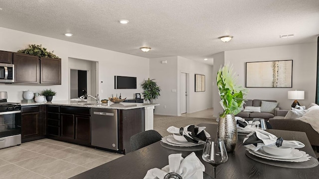 kitchen featuring visible vents, a peninsula, dark brown cabinets, open floor plan, and stainless steel appliances