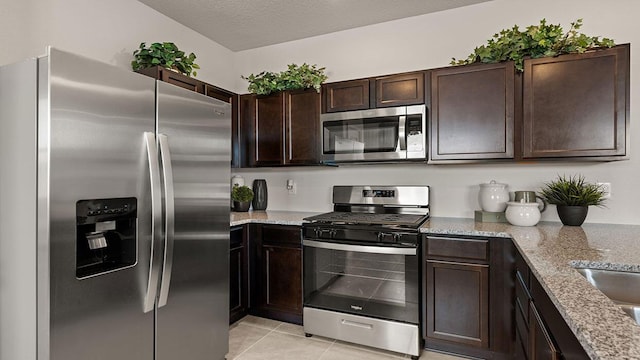 kitchen featuring dark brown cabinets, light stone countertops, a textured ceiling, appliances with stainless steel finishes, and light tile patterned floors