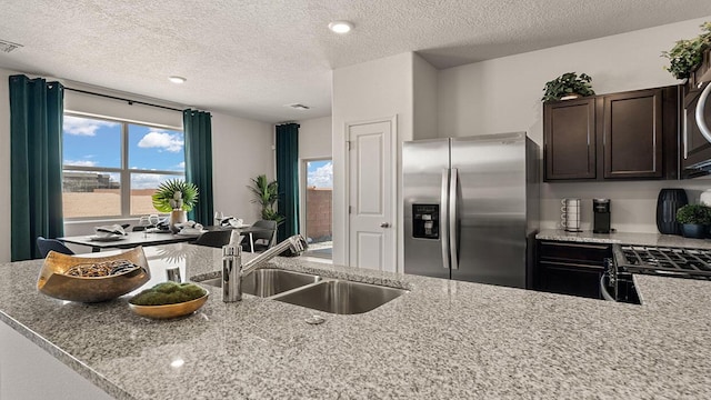 kitchen with dark brown cabinets, light stone counters, a sink, and stainless steel fridge with ice dispenser