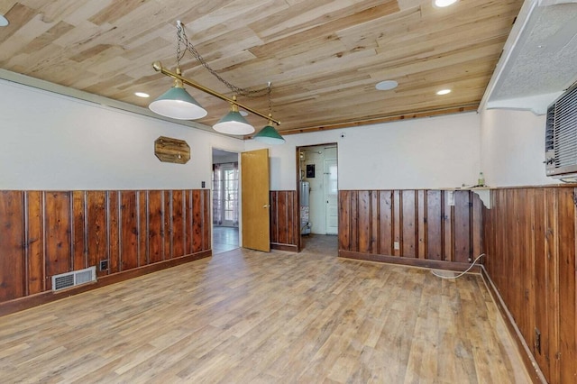 unfurnished room featuring visible vents, a wainscoted wall, wooden ceiling, wood walls, and wood finished floors