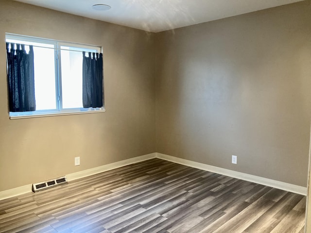spare room featuring visible vents, dark wood-style flooring, and baseboards