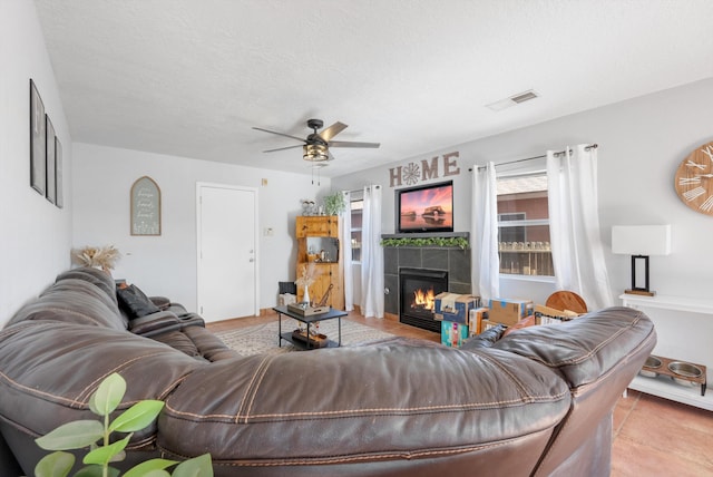 living area with a textured ceiling, a tiled fireplace, a ceiling fan, and visible vents
