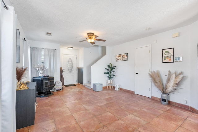 entryway with a wood stove, visible vents, a textured ceiling, and ceiling fan
