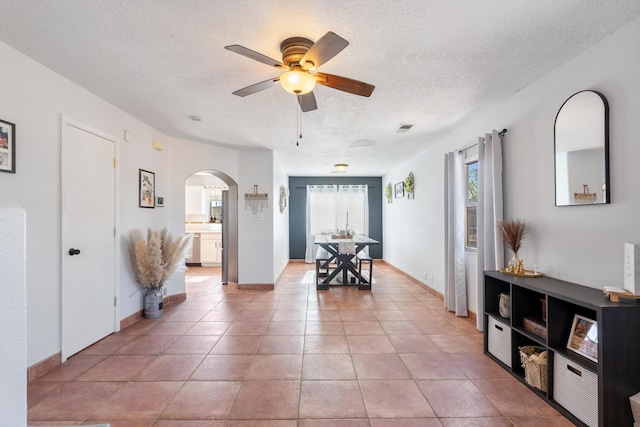 interior space featuring light tile patterned floors, a ceiling fan, arched walkways, and a textured ceiling