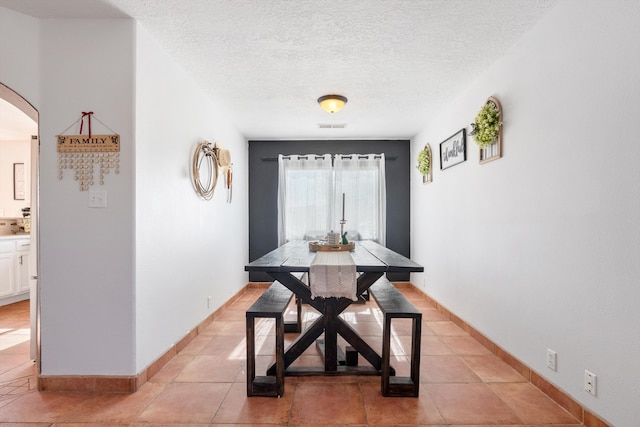 dining area featuring light tile patterned floors, arched walkways, a textured ceiling, visible vents, and baseboards