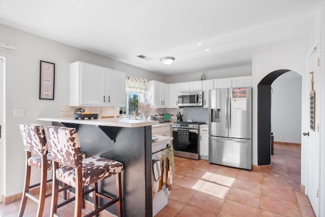 kitchen featuring a peninsula, backsplash, white cabinets, a kitchen bar, and stainless steel appliances