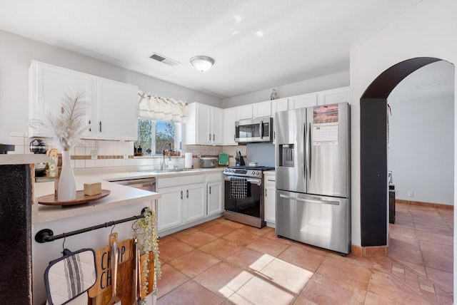 kitchen featuring tasteful backsplash, visible vents, arched walkways, a sink, and appliances with stainless steel finishes