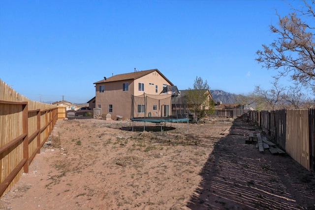 rear view of house featuring a fenced backyard, a trampoline, and stucco siding