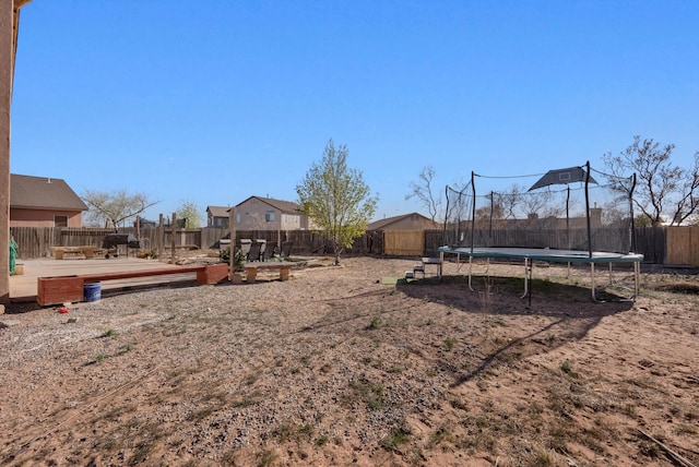 view of yard with a trampoline, a fenced backyard, and a deck