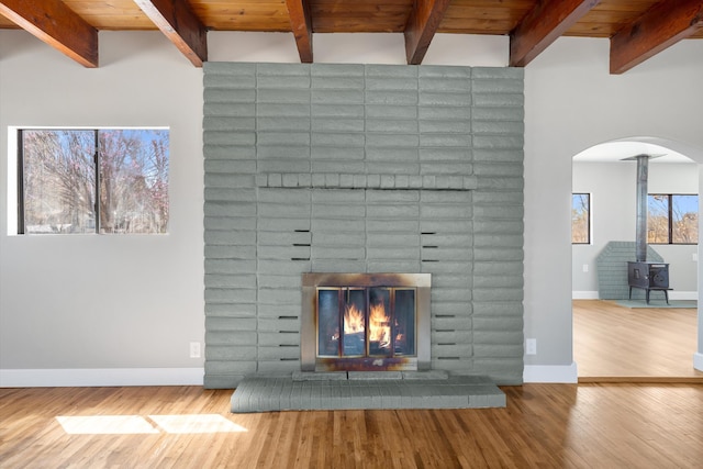 details featuring a wood stove, arched walkways, wood finished floors, a brick fireplace, and baseboards