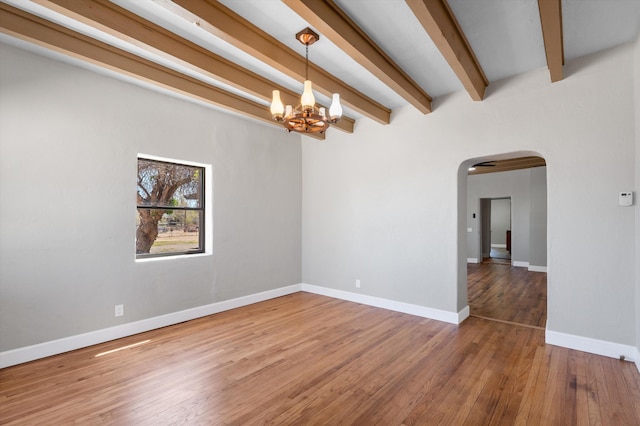 empty room with arched walkways, wood finished floors, baseboards, a notable chandelier, and beam ceiling