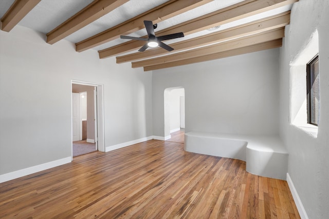 unfurnished room featuring arched walkways, baseboards, beamed ceiling, and wood finished floors