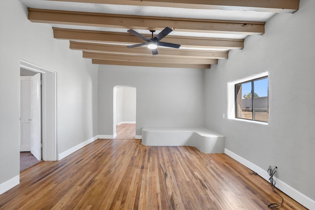 unfurnished room featuring arched walkways, baseboards, beamed ceiling, and wood finished floors