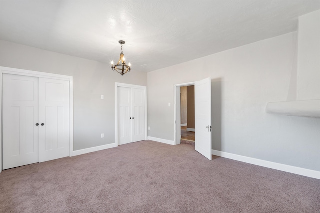 unfurnished bedroom featuring carpet floors, a notable chandelier, baseboards, and multiple closets