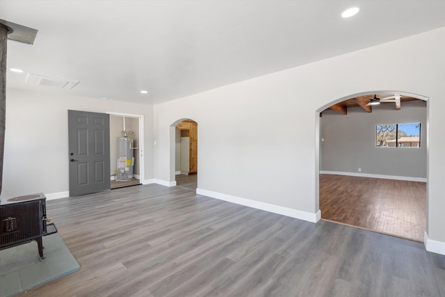 unfurnished living room featuring arched walkways, wood finished floors, baseboards, and gas water heater
