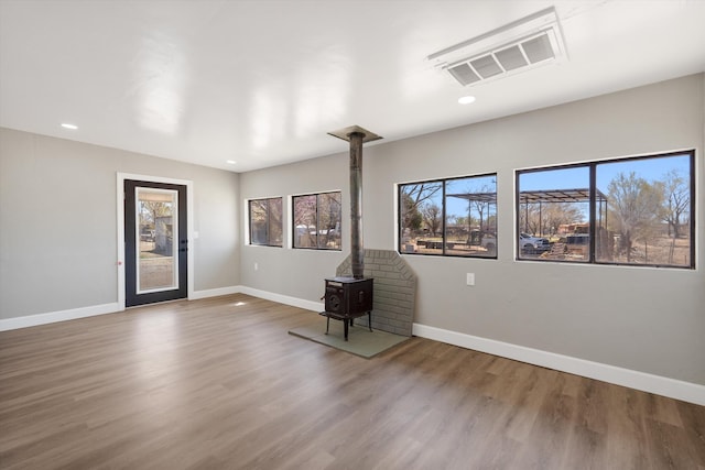 spare room featuring a wood stove, visible vents, recessed lighting, wood finished floors, and baseboards