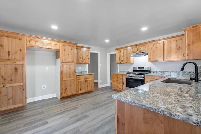 kitchen featuring light wood-type flooring, recessed lighting, under cabinet range hood, stainless steel gas stove, and a sink