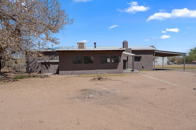 back of house featuring a carport, dirt driveway, metal roof, and stucco siding