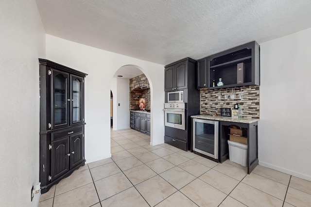 3008 Corona Dr NW, Albuquerque, NM 87120 - kitchen featuring appliances with stainless steel finishes, arched walkways, decorative backsplash, light tile patterned floors, and wine cooler