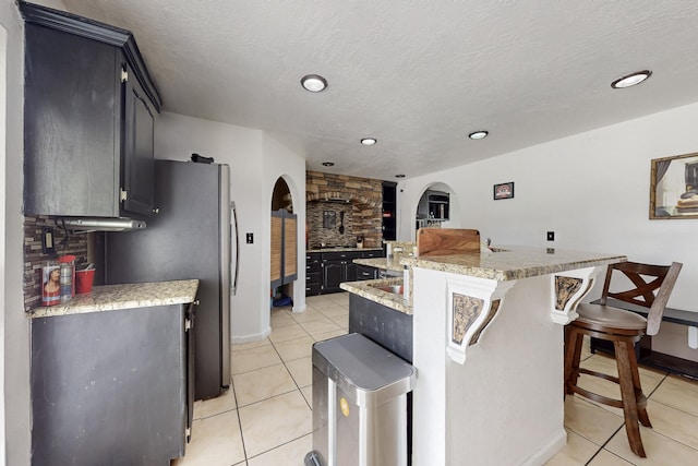 3008 Corona Dr NW, Albuquerque, NM 87120 - kitchen featuring a kitchen island with sink, arched walkways, baseboards, light tile patterned floors, and a kitchen bar