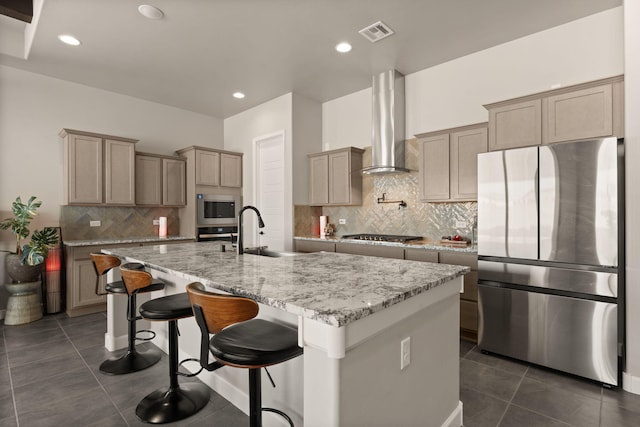 kitchen featuring wall chimney range hood, tasteful backsplash, a sink, stainless steel appliances, and visible vents