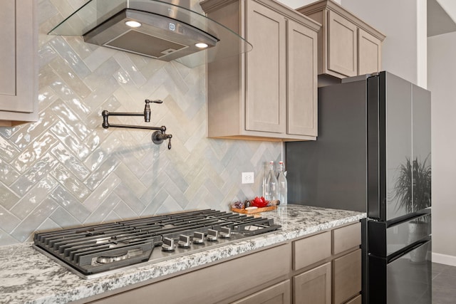 kitchen featuring backsplash, freestanding refrigerator, light stone countertops, and stainless steel gas cooktop