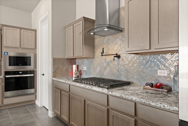 kitchen featuring decorative backsplash, wall chimney range hood, appliances with stainless steel finishes, and light stone counters