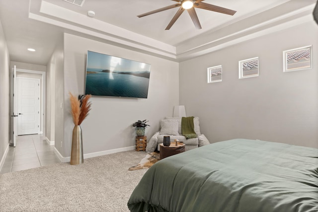 carpeted bedroom featuring tile patterned floors, baseboards, a raised ceiling, and ceiling fan