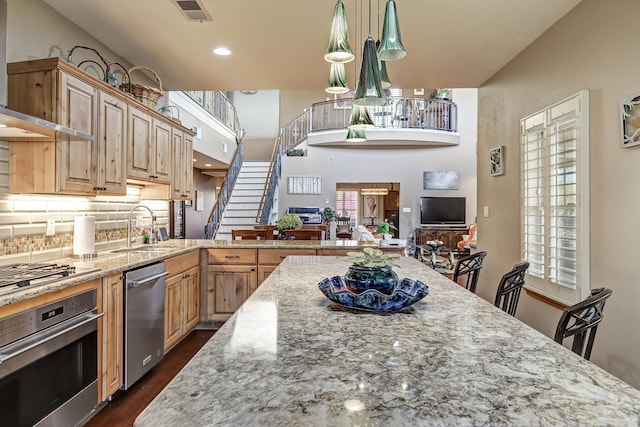 kitchen with visible vents, light stone countertops, a sink, stainless steel appliances, and wall chimney exhaust hood