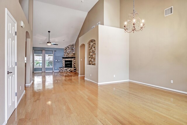 2703 Pueblo Grande Trl NW, Albuquerque, NM 87120 - unfurnished living room featuring visible vents, a stone fireplace, light wood-style flooring, arched walkways, and ceiling fan with notable chandelier