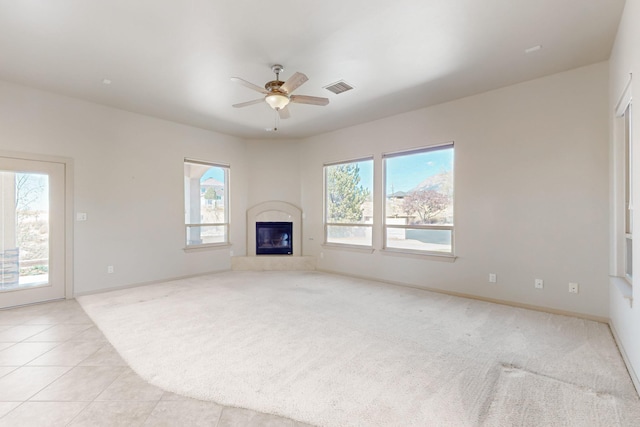 unfurnished living room with a glass covered fireplace, baseboards, a ceiling fan, and visible vents