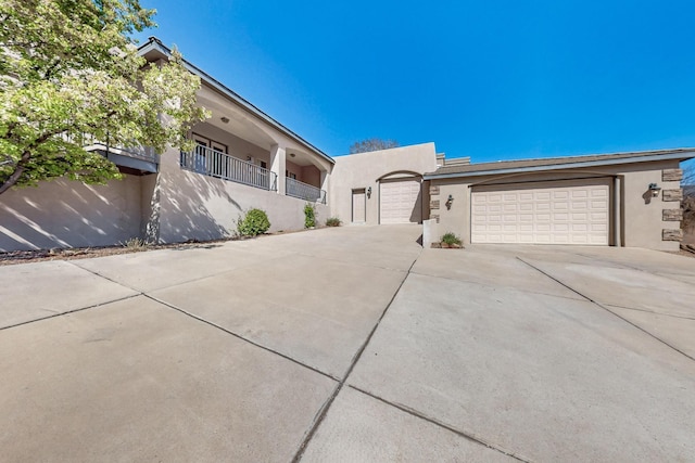 single story home featuring a garage, driveway, stucco siding, and a balcony