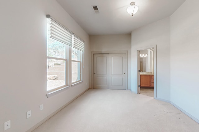 unfurnished bedroom with visible vents, baseboards, ensuite bathroom, a notable chandelier, and light carpet