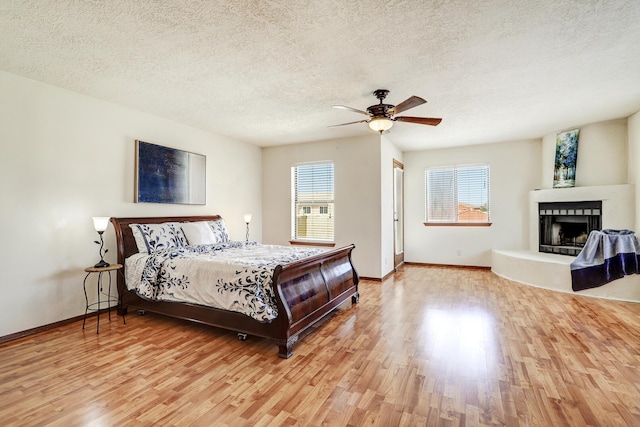 8300 R C Gorman Ave NE, Albuquerque, NM 87122 - bedroom with wood finished floors, a textured ceiling, a fireplace with raised hearth, and ceiling fan