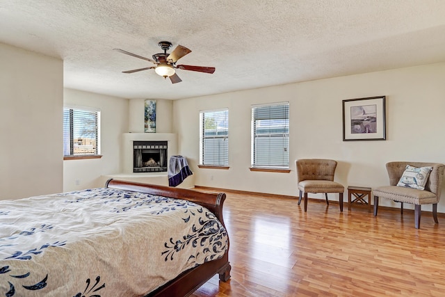 8300 R C Gorman Ave NE, Albuquerque, NM 87122 - bedroom featuring light wood-style floors, a fireplace with raised hearth, a textured ceiling, and ceiling fan