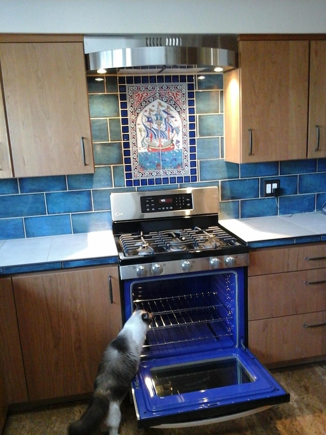 kitchen with wall chimney range hood, tasteful backsplash, stainless steel gas range, and light countertops