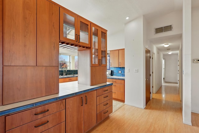 kitchen with glass insert cabinets, tasteful backsplash, visible vents, a sink, and light wood finished floors