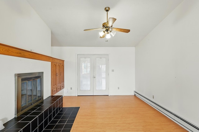 unfurnished living room featuring ceiling fan, a fireplace, wood finished floors, french doors, and a baseboard heating unit