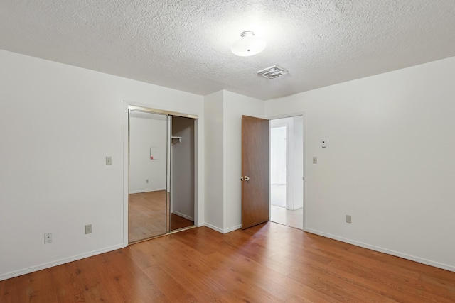 unfurnished bedroom featuring visible vents, baseboards, wood finished floors, and a textured ceiling