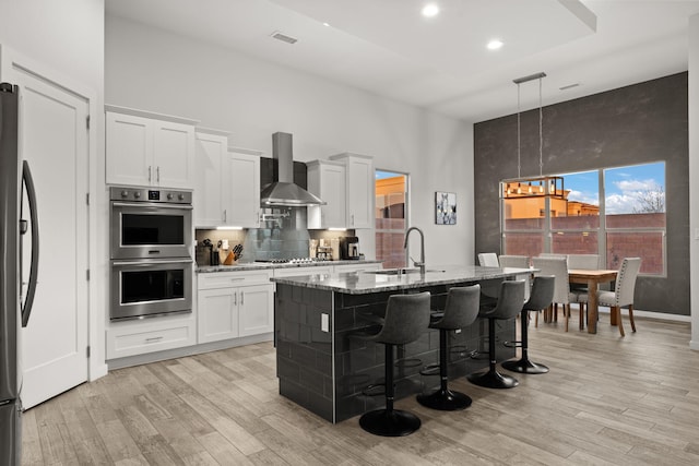 8023 Victoria Dr NW, Albuquerque, NM 87120 - kitchen with wall chimney range hood, light stone countertops, light wood-style flooring, stainless steel appliances, and a towering ceiling