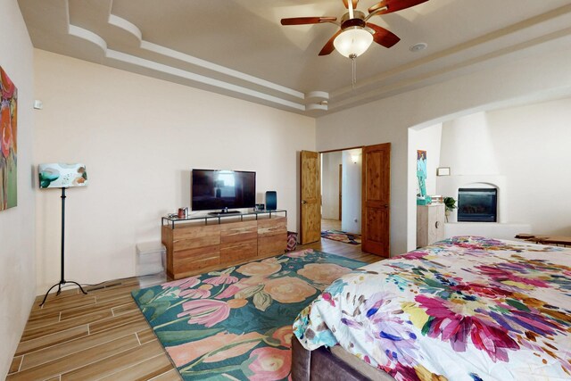 9840 Cameron St NW, Albuquerque, NM 87114 - bedroom featuring a ceiling fan, light wood-type flooring, a tray ceiling, a large fireplace, and arched walkways