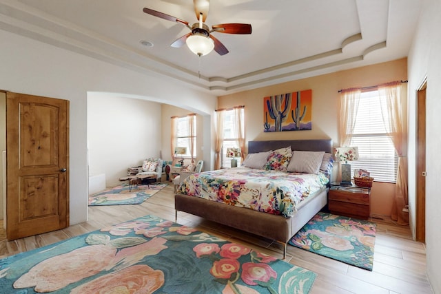 9840 Cameron St NW, Albuquerque, NM 87114 - bedroom with arched walkways, a ceiling fan, a tray ceiling, and light wood-style flooring