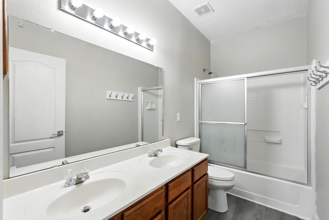 7327 Hearthstone Rd NW, Albuquerque, NM 87114 - full bath featuring toilet, wood finished floors, double vanity, combined bath / shower with glass door, and a textured ceiling
